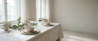 Minimalist dining table setup with beige linen tablecloth, ceramic dishware, and fresh greenery by bright windows. Scandinavian interior design for home decor and lifestyle content.