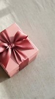 Pink gift box with satin ribbon bow on neutral linen background with natural window light shadows for holiday celebrations and special occasions.
