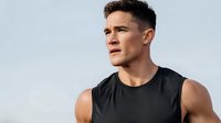 Athletic young Hispanic man in black tank top looking determined outdoors against clear sky background for fitness and sports content.
