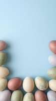 Colorful speckled Easter eggs arranged in decorative border frame on soft blue background with copy space for spring holiday greeting cards and designs.