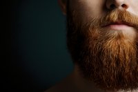 Close-up view of ginger beard and lips against dark background, showing facial hair texture and grooming details. Masculine portrait highlighting modern male style.