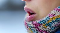 Close up profile of pink lips and colorful knitted winter scarf showing warmth and comfort in cold weather, soft focus macro photography with blurred background.