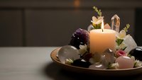 Healing crystals and gemstones arranged with burning candle and dried flowers in wooden bowl for meditation, spiritual wellness and energy cleansing.