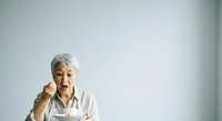 Senior Asian woman with white hair eating noodles with chopsticks against white background, suitable for food, lifestyle, and wellness content.
