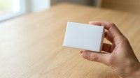 Close-up of hand holding blank white business card against wooden table background, suitable for branding and corporate identity mockups.