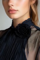 Close-up portrait of young woman wearing elegant black pleated blouse with decorative rose brooch, showing natural makeup lips and blonde hair against light background.
