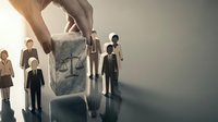 Hand selecting wooden block with justice scales symbol among business people figures representing legal decision making and corporate governance.