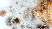 Macro photography of soap bubbles in orange and gray tones creating abstract pattern with depth and transparency. Artistic close-up shows delicate foam texture.