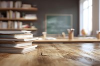 Stack of books on wooden desk in cozy classroom with chalkboard and bookshelves in background, creating warm educational atmosphere.