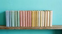 Row of vintage books with pastel colored spines arranged on wooden shelf against turquoise wall for home decor and reading concepts.