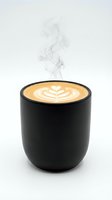 Hot cappuccino with latte art in black ceramic cup, steam rising against white background. Perfect for coffee shop, café, beverage, and hospitality design projects.