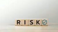 Wooden blocks spelling RISK with blue shield checkmark symbol representing business security, risk management and protection strategies for corporate planning.