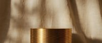 Golden cylindrical podium with ridged texture on beige linen background with soft shadow overlay for luxury product display.
