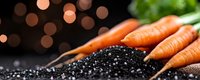Fresh organic carrots with green tops lying on black soil with water drops against dark background with bokeh lights, macro food photography.
