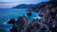 Dramatic rocky coastline with towering cliffs overlooking turquoise ocean waters at twilight, featuring jagged rock formations and coastal landscape for travel and nature design projects.