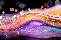 Macro photography of colorful liquid waves with water drops and bokeh effects creating an abstract artistic composition in orange, purple, and blue tones.