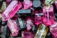 Raw tourmaline crystals in vibrant pink, black, and green colors showing natural mineral formation, texture and transparency. Close up macro photography.