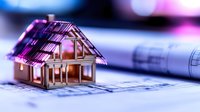 Miniature golden house model on architectural blueprints with soft pink and blue bokeh lighting effect creates dreamy real estate concept background.