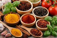 Colorful spices and herbs in wooden bowls with fresh vegetables on rustic table for cooking and seasoning culinary preparations.