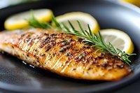 Grilled salmon fillet with crispy skin, fresh rosemary sprigs and lemon slices served on black plate, close up view showing juicy texture and caramelized surface.