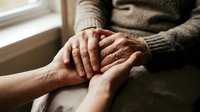 Elderly hands holding younger hands in warm light showing intergenerational care, support and family connection between senior and adult person.