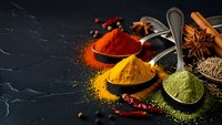 Colorful spices in wooden spoons on dark slate background. Paprika, turmeric, green powder with cinnamon sticks and star anise for cooking and seasoning.