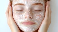 Young woman with closed eyes enjoying facial scrub treatment, hands gently touching face during skincare routine for healthy glowing skin and relaxation.