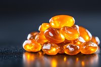 Fresh orange fish oil or omega-3 capsules on dark background with water drops. Vitamin D supplement pills with golden translucent glow for health concept.