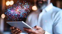 Digital transformation concept with glowing particles emerging from tablet device held by professional in white shirt against blurred background.