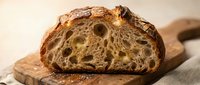 Freshly baked artisan sourdough bread loaf with open crumb structure, sliced and displayed on wooden board for bakery, food photography, and culinary content.