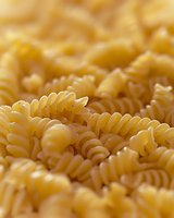 Uncooked fusilli pasta macro shot showing spiral shape and texture of traditional Italian durum wheat noodles in warm golden color for food background.