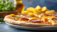Fresh homemade pizza with pepperoni, melted cheese and yellow bell peppers on white ceramic plate against rustic blue background, selective focus on toppings.