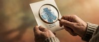 Senior man examining vintage medical caduceus symbol through magnifying glass for healthcare research and historical medical study purposes.