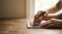 Senior man's hands using smartphone on wooden floor in warm sunlight, technology and aging concept for digital literacy and connectivity.