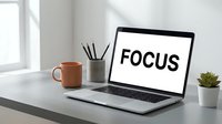 Modern laptop displaying FOCUS text on screen sits on clean white desk with coffee mug, pencil holder and small plant in bright office workspace for productivity.