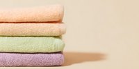 Stack of folded pastel colored towels in peach, cream, mint green, and lavender on neutral beige background, creating soft minimalist composition.
