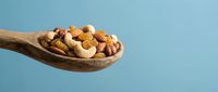 Mixed nuts and dried fruits in wooden spoon on blue background. Healthy snacking, protein-rich food for nutrition and wellness lifestyle.