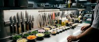 Professional chef preparing fresh ingredients in commercial restaurant kitchen with knife collection and colorful mise en place bowls ready for cooking service.