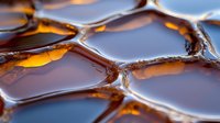 Macro shot of golden honey in honeycomb cells showing natural geometric pattern, liquid texture and amber color. Sweet organic food background.