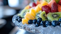 Fresh colorful fruit platter with strawberries, blueberries, kiwi, and mango arranged on crystal serving dish, selective focus on juicy berries and tropical fruits.
