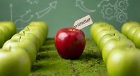 Red apple with leadership flag standing out among green apples on moss surface with business growth arrows and gears background for teamwork concepts.