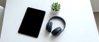 Modern workspace setup with black tablet, wireless headphones and small succulent plant on clean white desk for productivity and remote work.