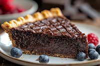 Rich chocolate tart slice with golden pastry crust garnished with fresh blueberries and raspberries on white plate for dessert menu and bakery advertising.