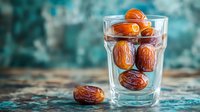 Fresh organic Medjool dates in clear glass on rustic wooden table against blurred turquoise background, healthy natural dried fruit snack for dessert.