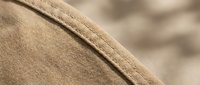 Close-up macro shot of beige fabric texture with detailed stitching seam, showcasing textile craftsmanship and material quality for fashion design projects.