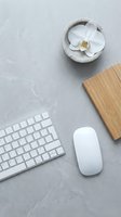 Minimalist workspace with white orchid flower in stone bowl, wireless keyboard, mouse and bamboo notebook on concrete surface for office design.