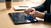 Professional businessman analyzing financial data and stock market charts on digital tablet at modern office desk with coffee and notebook nearby.
