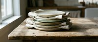 Stack of rustic ceramic plates with linen napkins on weathered wooden table, suitable for tableware, dining, and home decor styling.