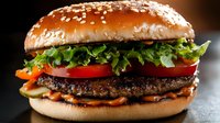 Juicy beef burger with fresh lettuce, tomato and sesame seed bun on dark background. Fast food restaurant menu item for advertising and promotional materials.