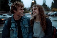 Young couple laughing together outdoors at dusk, wearing casual denim and backpacks, sharing authentic moment of joy in urban parking lot setting.
